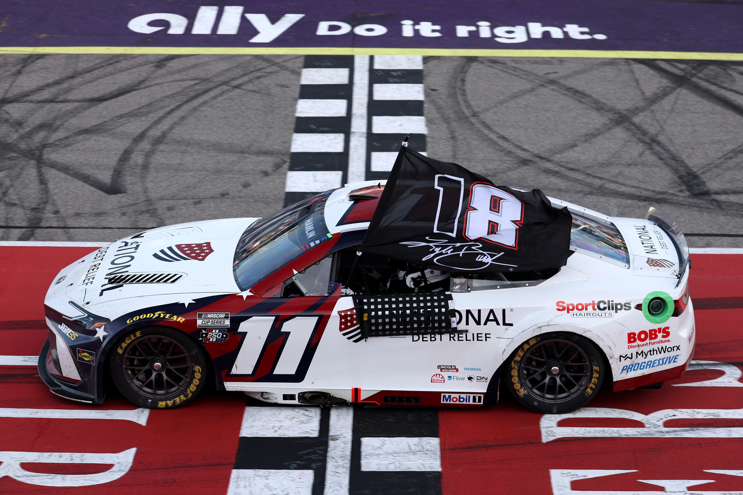 BROOKLYN, MICHIGAN - JUNE 07: Denny Hamlin, driver of the #11 National Debt Relief Toyota, waves an 18 - 8 flag in honor of the late Kyle Busch after winning the NASCAR Cup Series FireKeepers Casino 400 at Michigan International Speedway on June 07, 2026 in Brooklyn, Michigan. (Photo by Brett Farmer/Getty Images)